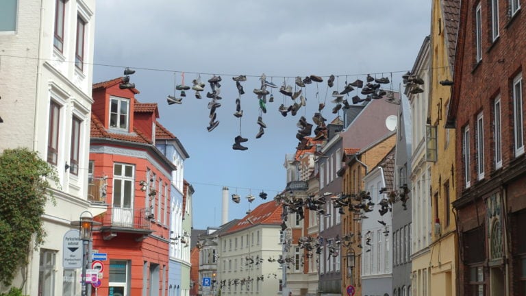 Schuhe baumeln über einer Leine in der Norderstraße in Flensburg. Warum sie das tun? Weiß niemand so genau. Aber es gibt viele Ideen.