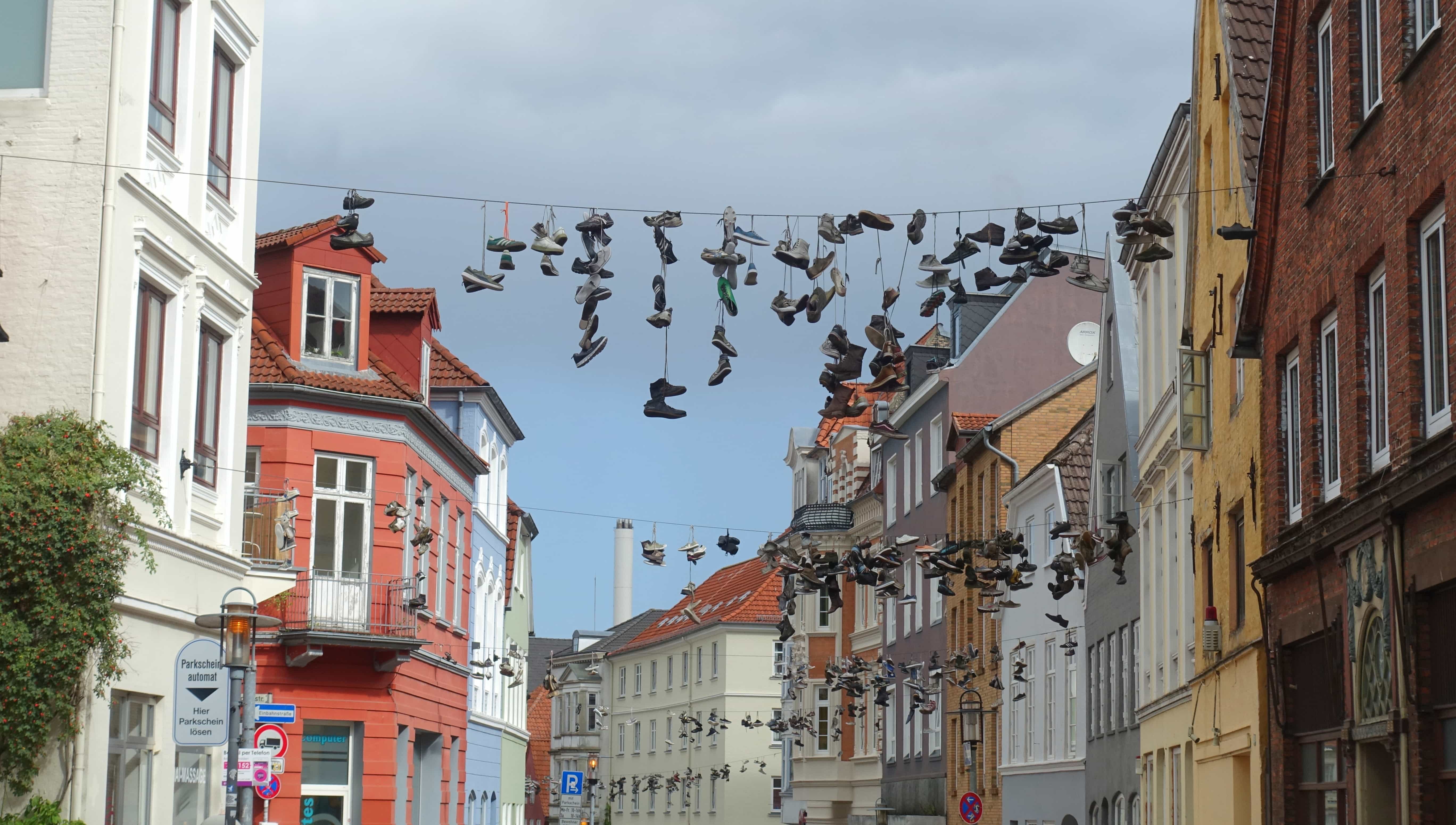 Schuhe baumeln über einer Leine in der Norderstraße in Flensburg. Warum sie das tun? Weiß niemand so genau. Aber es gibt viele Ideen.