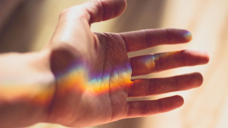 Ein Regenbogen erscheint inmitten einer geöffneten Handfläche