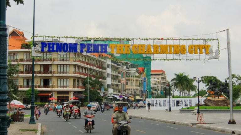 Charmin City steht über der Straße von Phnom Penh, darunter Rollerfahrer.