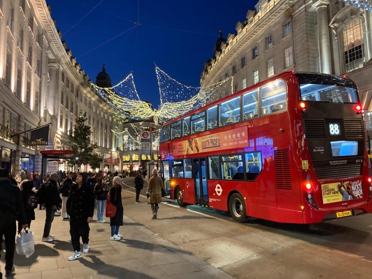 In den vielen Einkaufsstraßen in London hängen winterliche Lichter, zum Beispiel leuchtende Engel in der Regent Street. Ein roter Bus fährt vorbei.