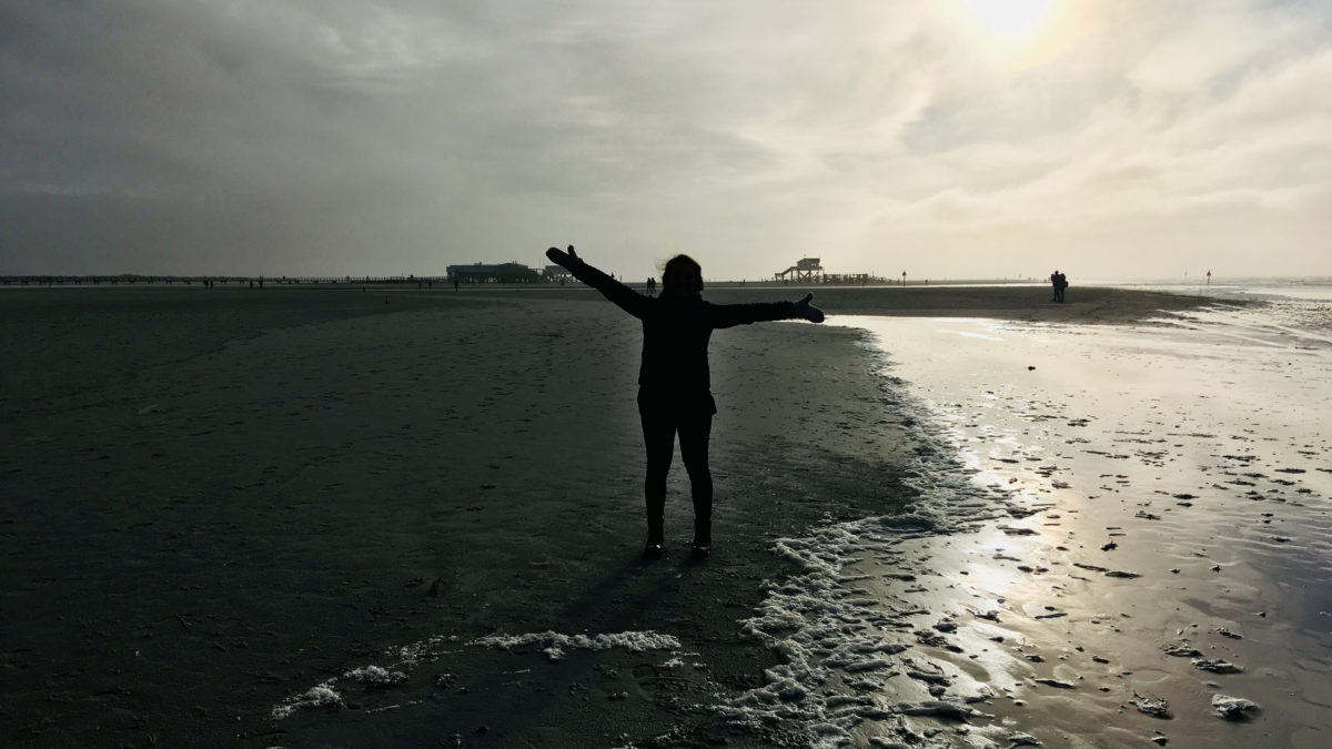 Julia steht mit gehobenen Armen am Strand von Sankt Peter Ording in Nordfriesland