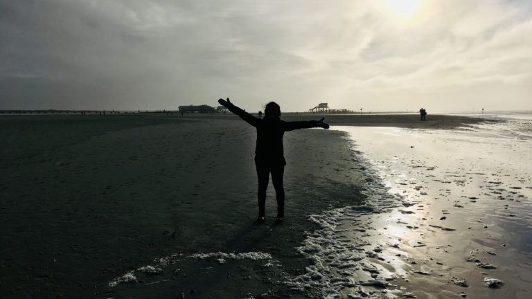 Julia steht mit gehobenen Armen am Strand von Sankt Peter Ording in Nordfriesland