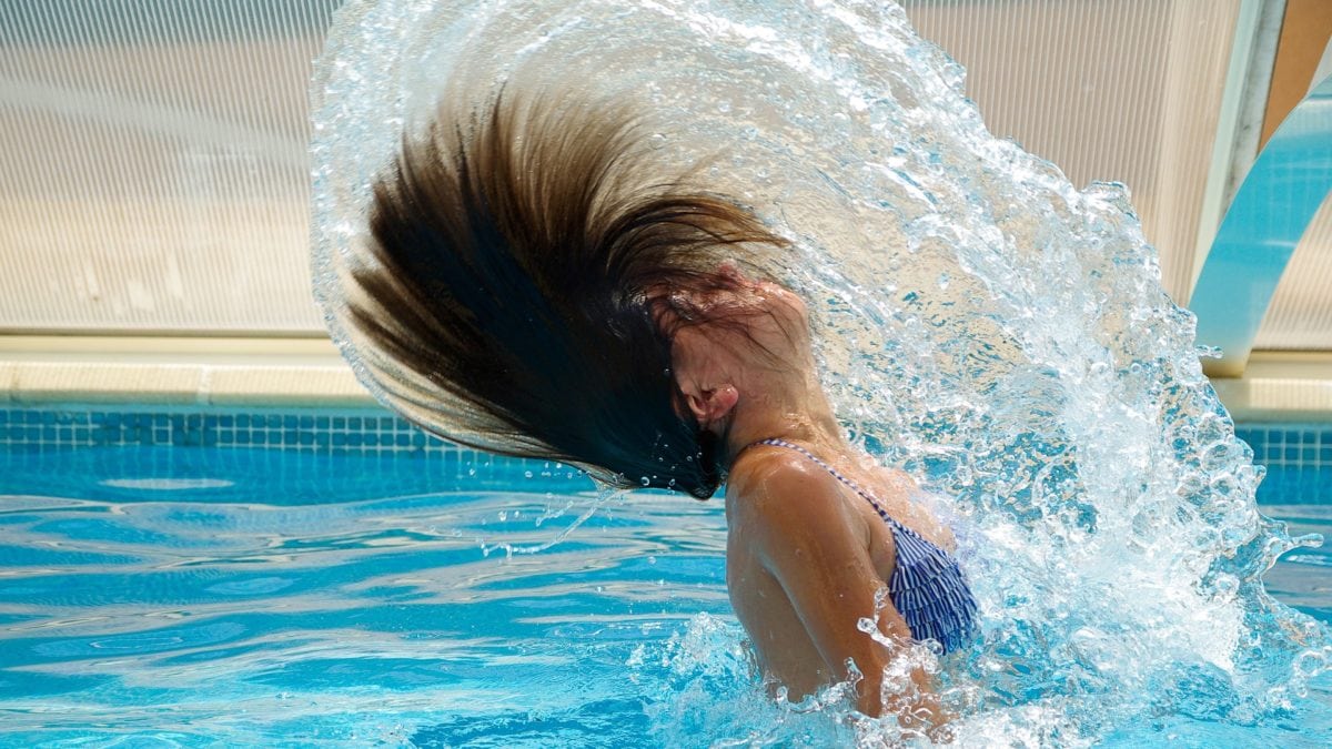 Mädchen im Schimmbad taucht aus dem Pool auf und schwingt Haare über den Kopf