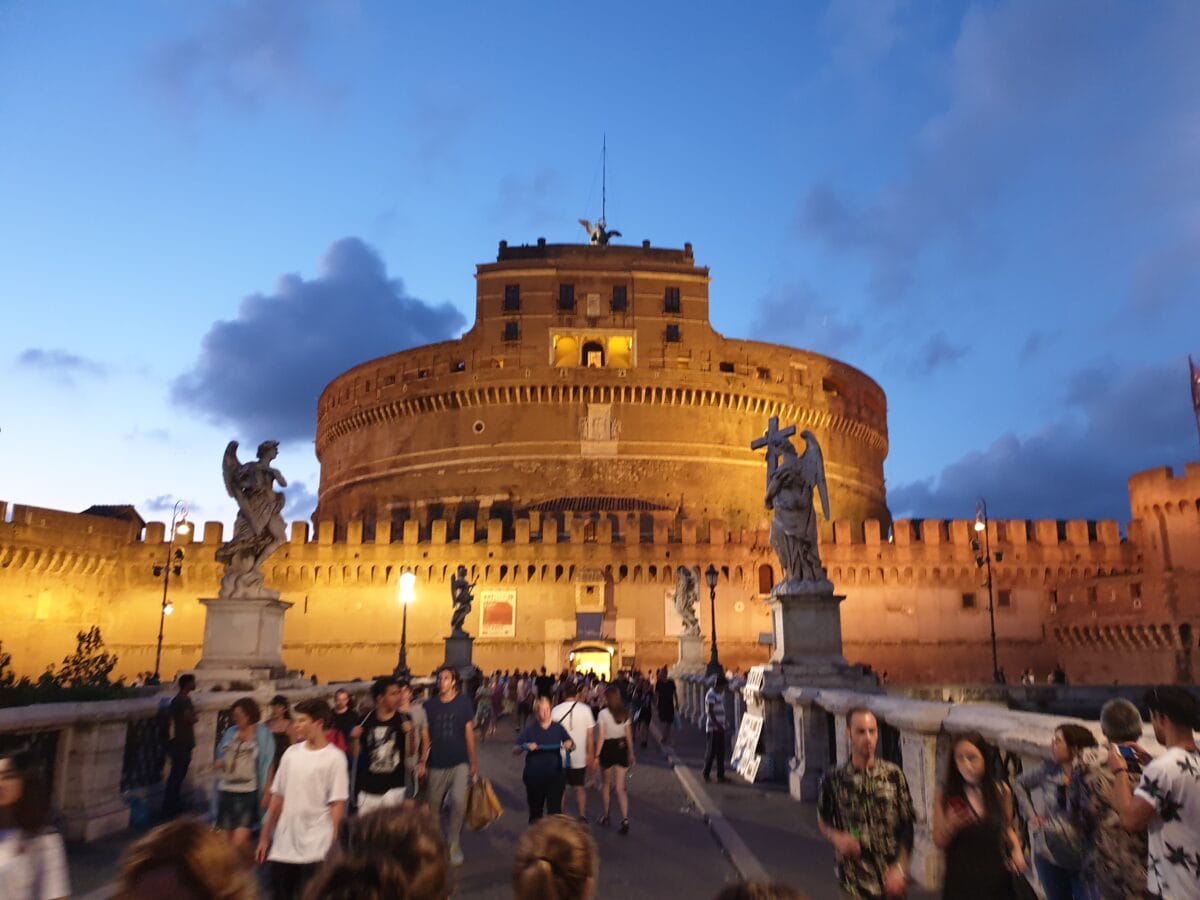 Die Engelsburg in Rom steht im Abendlicht hell erleuchtet am Tiber am Ende der Engelsbrücke. 