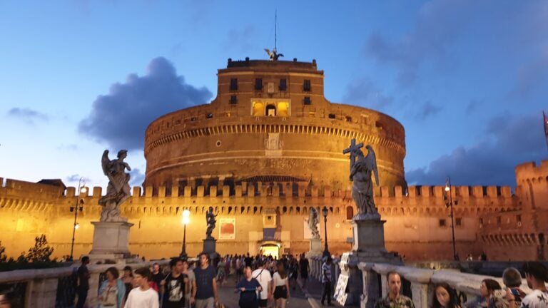 Die Engelsburg in Rom steht im Abendlicht hell erleuchtet am Tiber am Ende der Engelsbrücke.