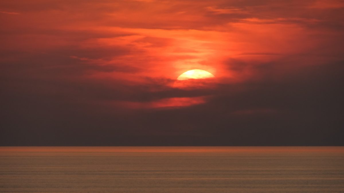 Die Sonne verschwindet über dem Meer rötlich hinter Wolken in der Nacht