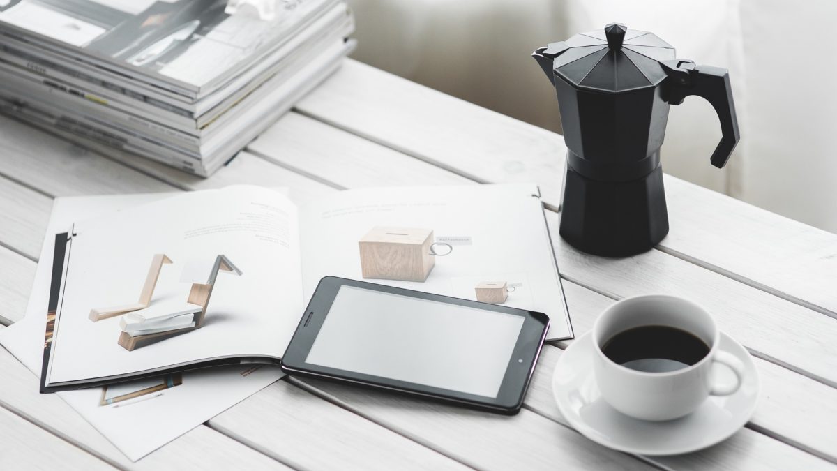 Arbeitsmaterialien liegen neben einer vollen Kaffeetasse und einer Kanne auf einem Schreibtisch, ein normaler Tag im Büro