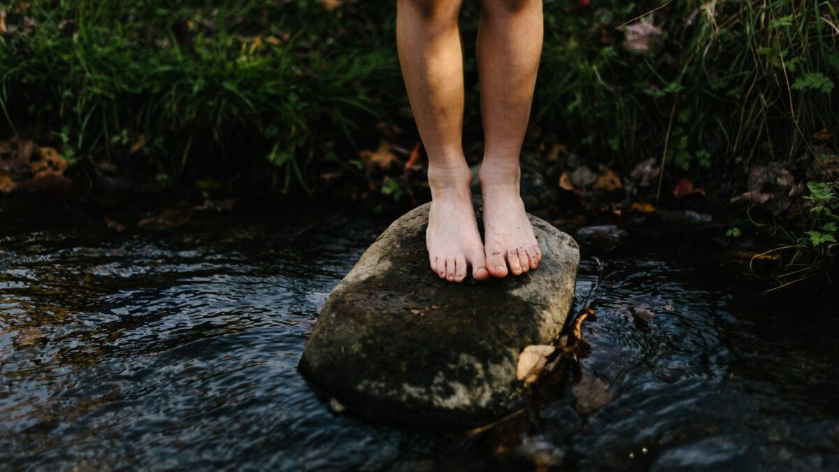 Ein paar Füße stehen barfuß auf einem Stein im Fluss